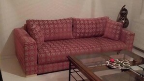 Un sofá con estampado geométrico, una mesa de centro de cristal y un objeto decorativo en la pared.