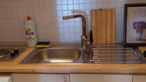 Una cocina con un lavamanos de acero inoxidable, una tabla de cortar de madera y una botella de detergente.