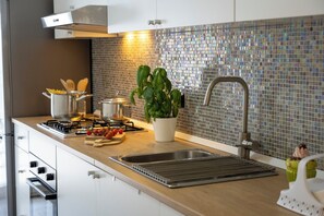 A modern kitchen with a stainless steel sink, a gas stove, and a backsplash of reflective tiles.