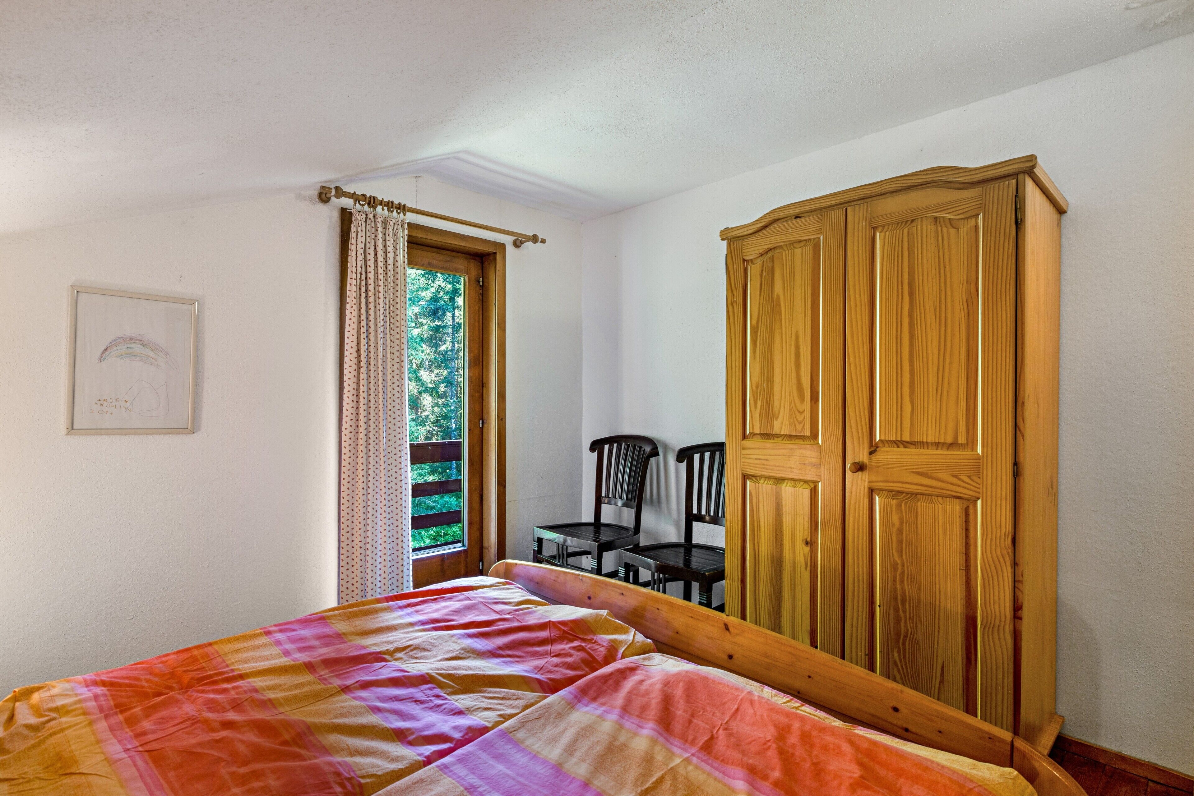 Ein Schlafzimmer mit einem Bett, einem Holzschrank, einem Fenster mit Vorhängen und einem Sessel.