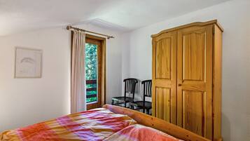 Ein Schlafzimmer mit einem Bett, einem Holzschrank, einem Fenster mit Vorhängen und einem Sessel.
