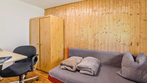 Una habitación con pared de paneles de madera, un escritorio con una silla y un sofá con una manta.