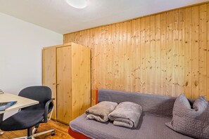 A room with a wooden panel wall, a desk with a chair, and a sofa with a blanket.