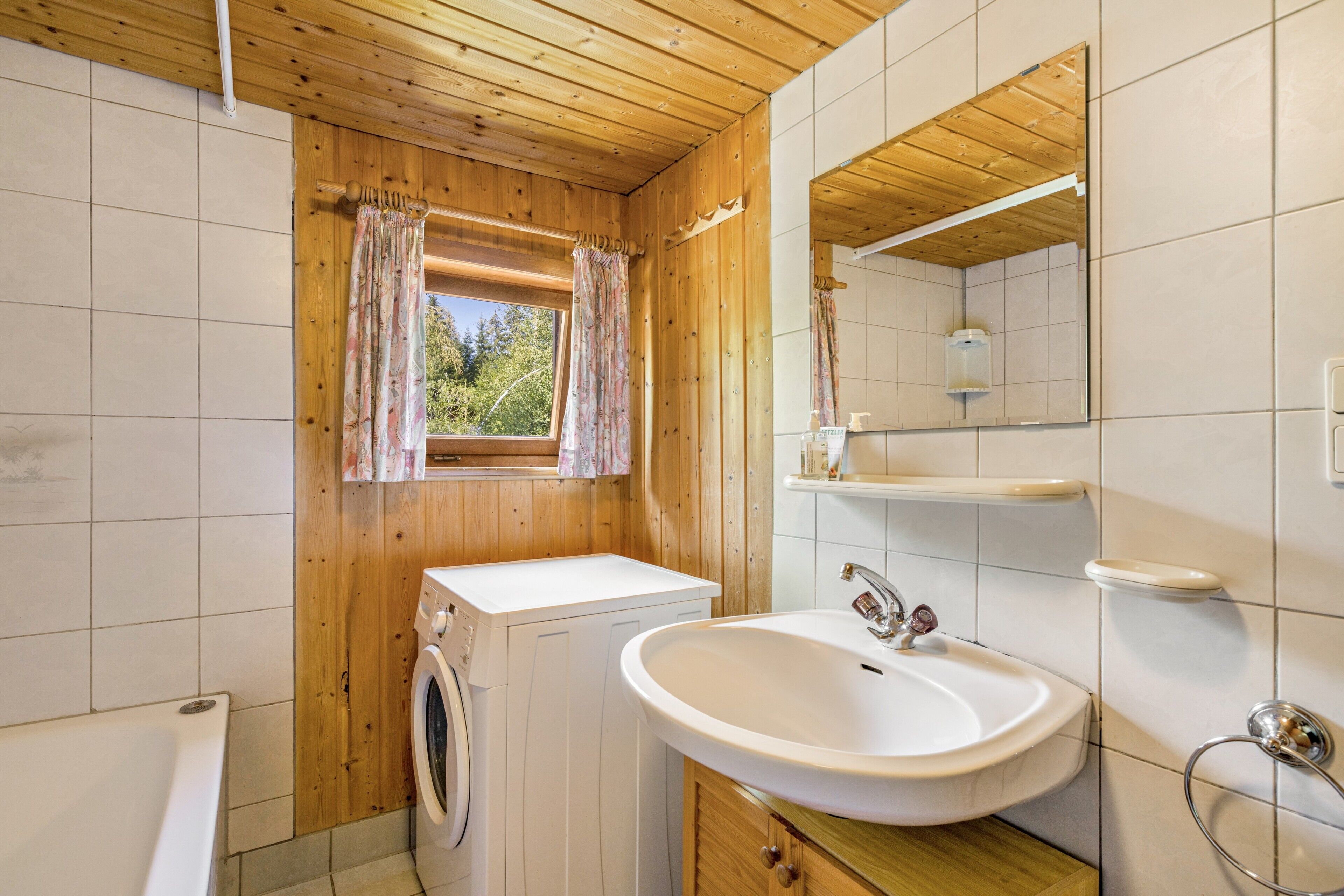 Ein kleines Badezimmer mit Holzboden, einer Waschmaschine, einem Waschbecken und einem Spiegel.