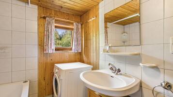 Ein kleines Badezimmer mit Holzboden, einer Waschmaschine, einem Waschbecken und einem Spiegel.