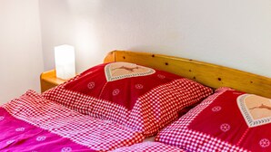 Una cama con una manta y almohadas a cuadros, un cabecero de madera y una mesita de noche con una lámpara.