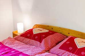 A bed with a checkered blanket and pillows, a wooden headboard, and a bedside table with a lamp.