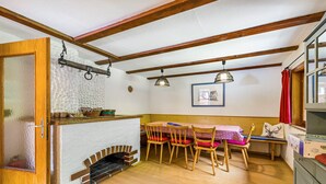 Una habitación acogedora con techo de madera, chimenea, una mesa de comedor con sillas y una ventana con cortina roja.
