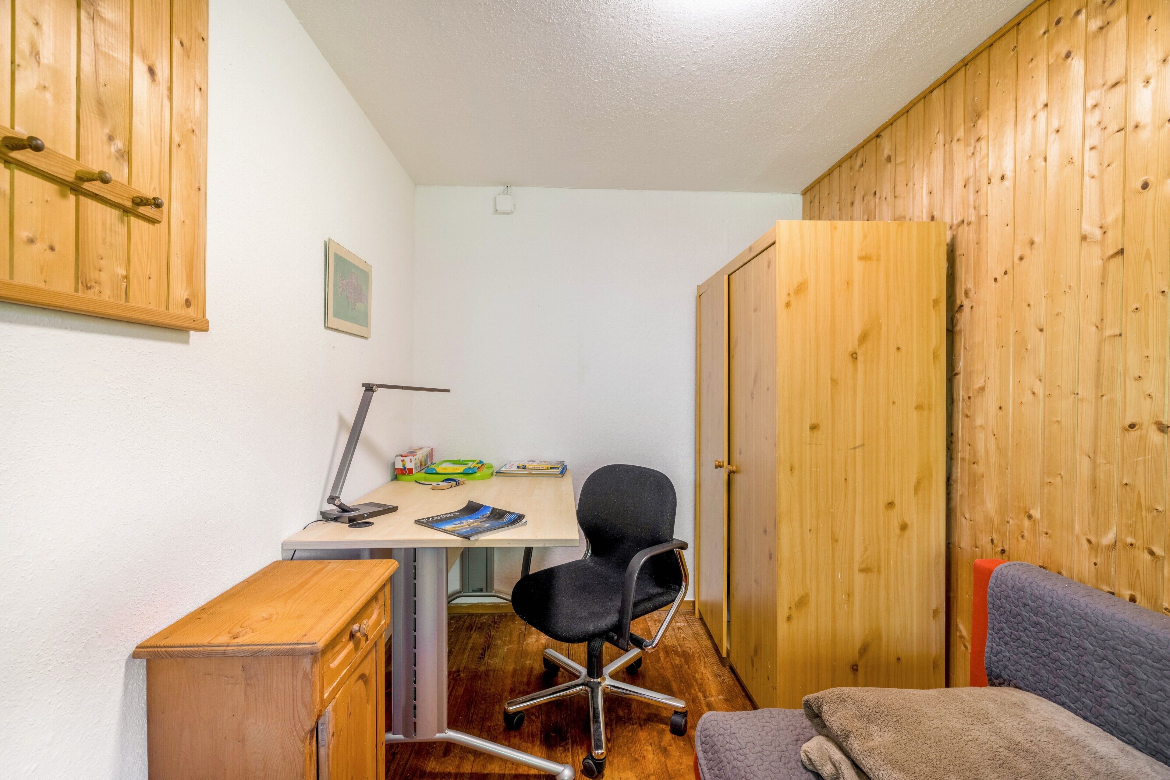 Een kleine, knusse kamer met een houten bureau, een stoel en een bed.