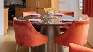 Uma cozinha moderna com armários de madeira, uma mesa de jantar com cadeiras laranja e uma janela com cortinas vermelhas.