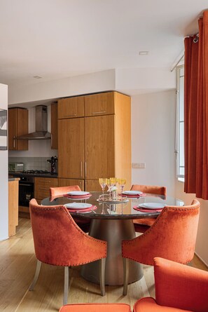 A modern kitchen with wooden cabinets, a dining table with orange chairs, and a window with red curtains. - pollen · Spacious 2-bedroom apartment in Mayfair (London)