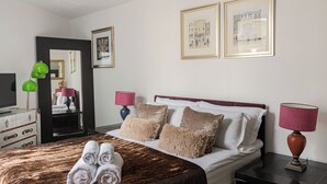 Quarto de hotel com cama, duas luminárias laterais, penteadeira, espelho e quadros na parede.