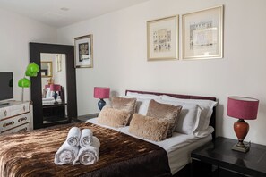 A hotel room with a bed, two bedside lamps, a dresser, a mirror, and framed pictures on the wall. - pollen · Spacious 2-bedroom apartment in Mayfair (London)