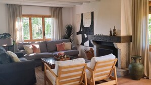 Een woonkamer met een bank, stoelen, een open haard en een groot abstract schilderij.