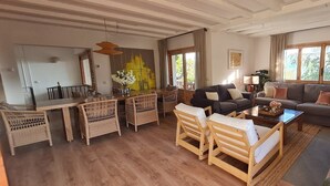 Een ruime woonkamer met een eettafel, rieten stoelen, een bank en een salontafel.