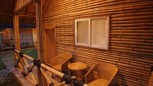 A log cabin with a thatched roof, a window, and wicker furniture. - Maharsh Bamboo Stays near Devanahalli Deluxe Room (Doddacheemanahalli)