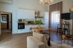 Eine moderne Küche mit weißen Schränken, ein Essbereich mit rundem Tisch und ein Wohnzimmer mit einer Couch.