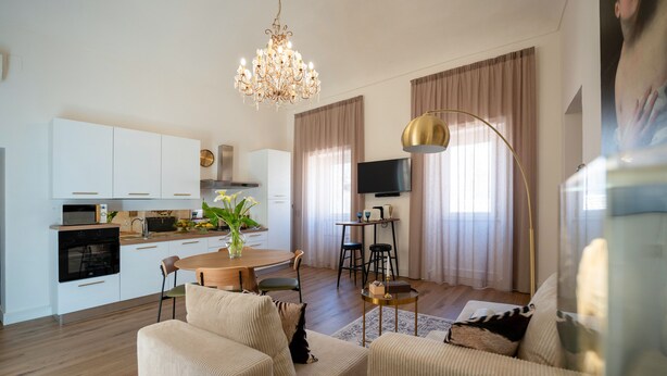 En moderne stue med sofa, spisebord og et køkkenområde med hvide skabe og et fjernsyn.