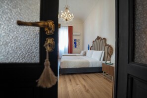 Ein Schlafzimmer mit einem Bett, einer Kristallleuchter, Holzboden und einer Tür mit Messingklinke.