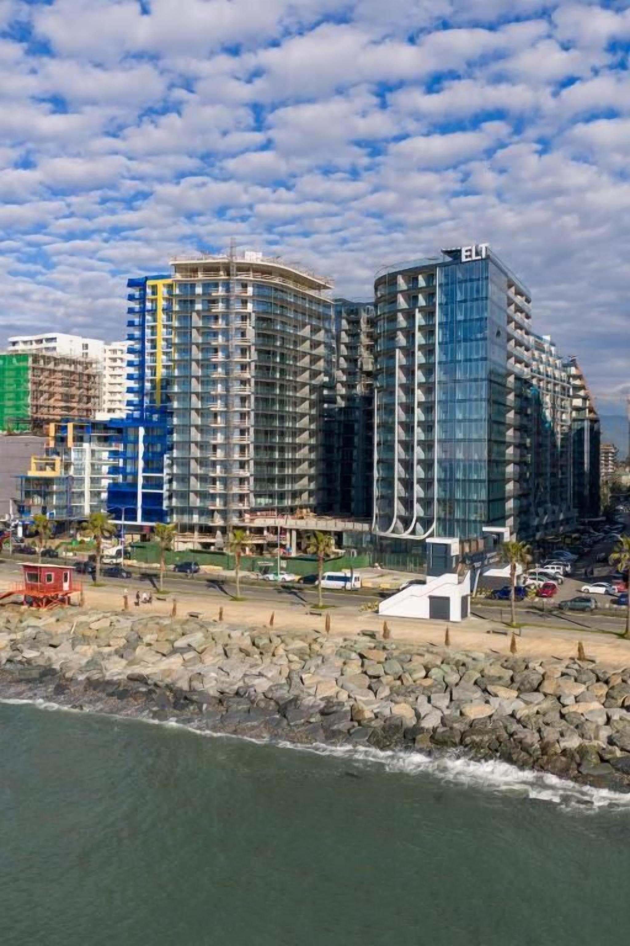 Un hotel de gran altura con varios balcones, ubicado junto a una costa rocosa y vista al océano.