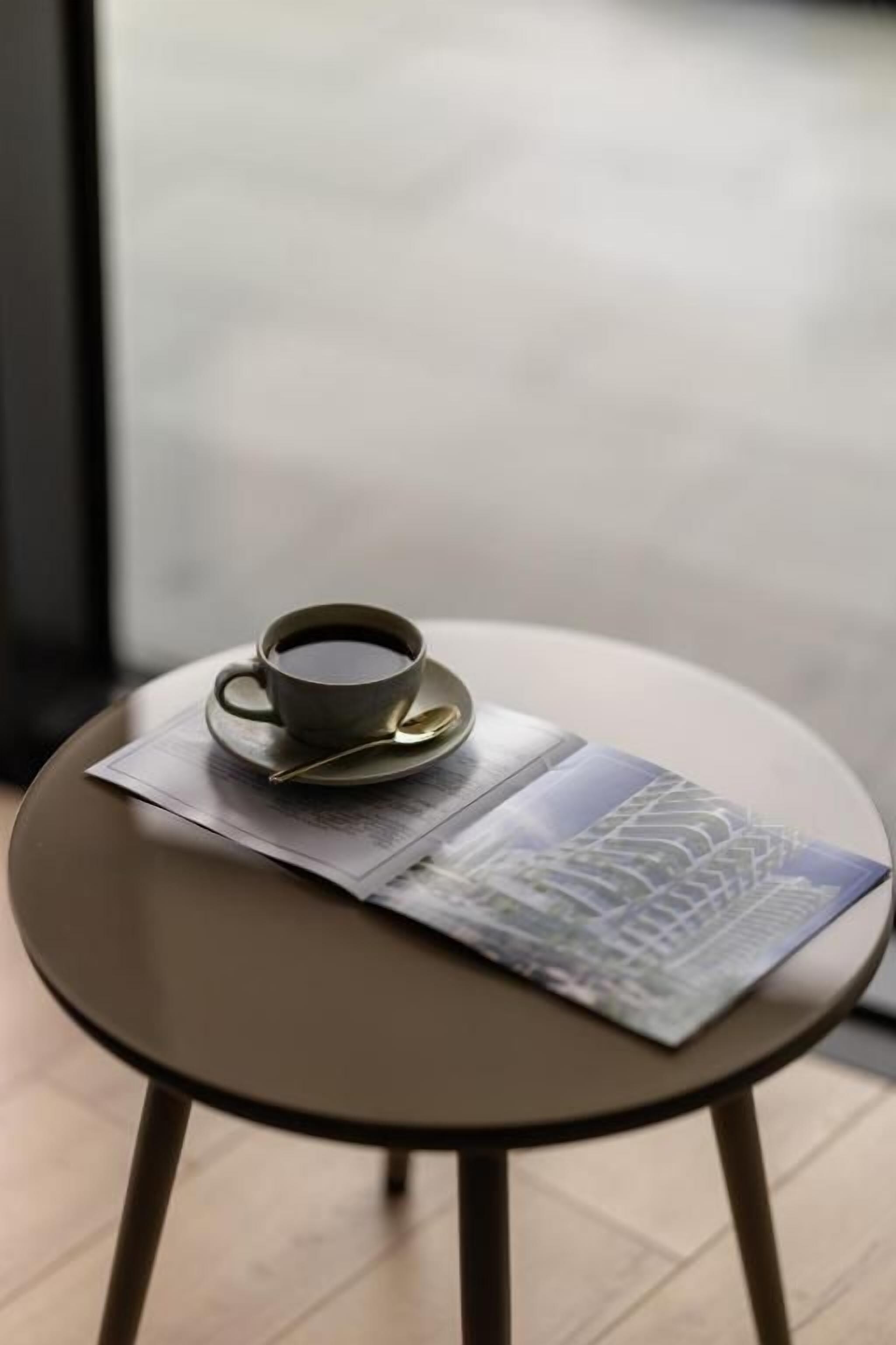A table with a cup and saucer, a magazine, and a spoon.
