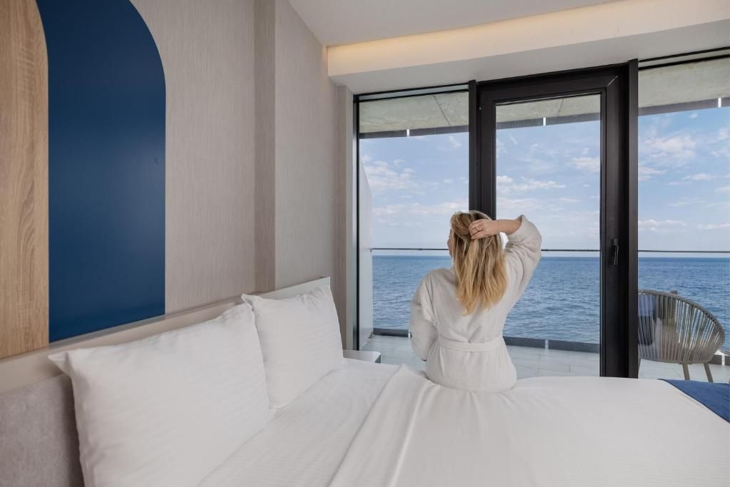 Une chambre avec un grand lit, une vue sur la mer par une porte vitrée et un fauteuil près de la fenêtre.
