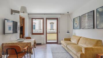 Ein Essbereich mit Tisch für vier Personen, einer Couch und einem großen Fenster mit Blick auf Gebäude.