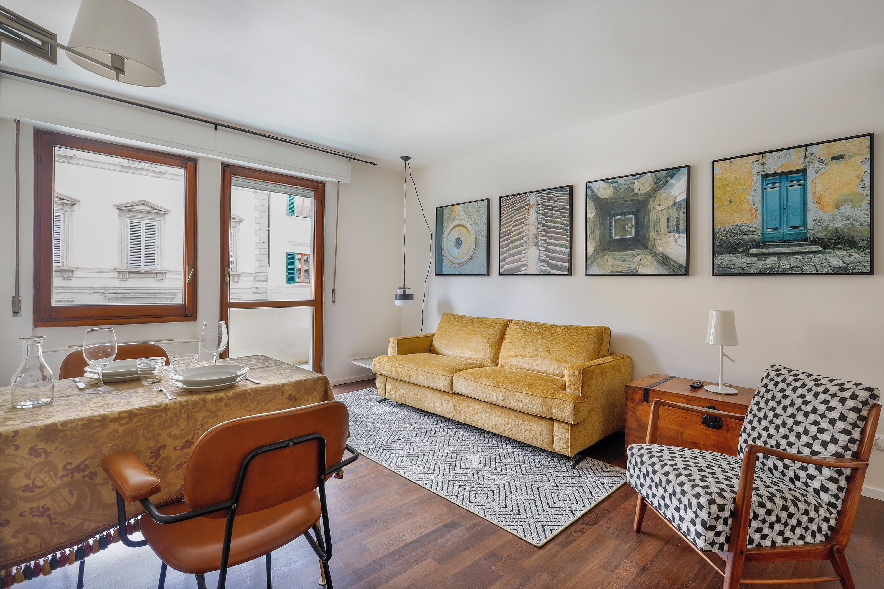 A dining area with a table set for four, a sofa, a patterned armchair, and artwork on the walls.