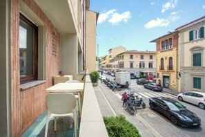 A balcony with a table and chairs, a row of parked motorcycles, and a street view with cars and buildings. - Sara Studio Apartment (Florence)