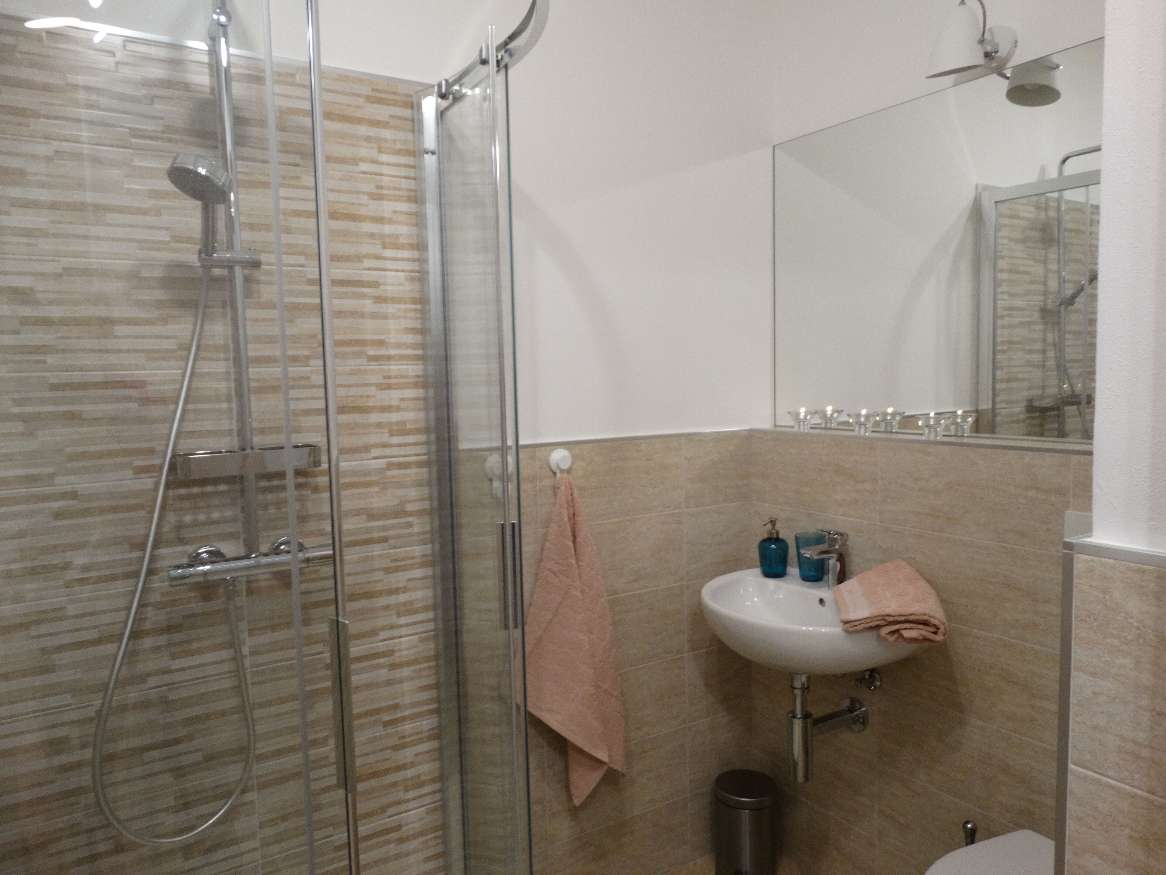 Een badkamer met een douchecabine van glas, een wastafel met spiegel en een toilet.
