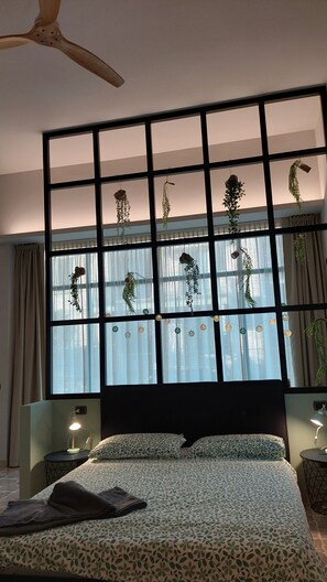 Un dormitorio con cama, ventilador de techo, ventana con cortinas y una lámpara fijada a la pared.