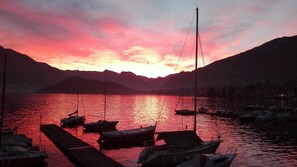 Un coucher de soleil sur un lac paisible, avec des bateaux amarrés à un quai, le tout entouré de montagnes.
