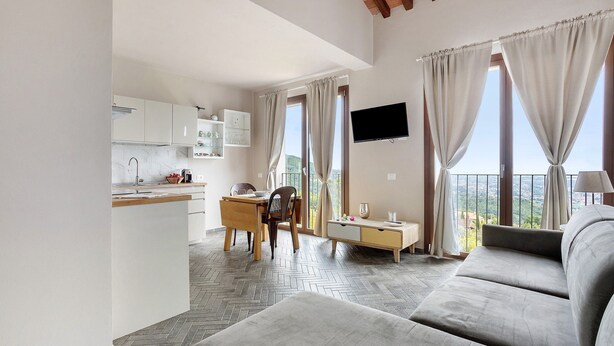 A modern living room with a sofa, a dining area with a table and chairs, a kitchen with cabinets, and a TV mounted on the wall. - Apartment 'A Fosdinovo' with Mountain View, Wi-Fi and Air Conditioning (Fosdinovo)