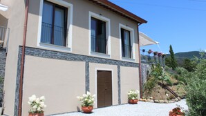A two-story building with a beige facade, a brown door, and two windows with white frames. There are potted plants in front of the building. - Apartment 'A Fosdinovo' with Mountain View, Wi-Fi and Air Conditioning (Fosdinovo)