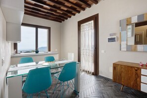 Zona pranzo con tavolo in vetro, sedie color acquamarina, un mobiletto in legno e vista dalla finestra.