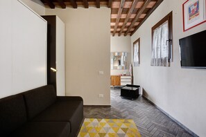 A living room with a sofa, a patterned rug, a TV, and a kitchen in the background. - Apartment 'Incantevole - Fosdinovo' with Mountain View, Wi-Fi and Air Conditioning (Fosdinovo)