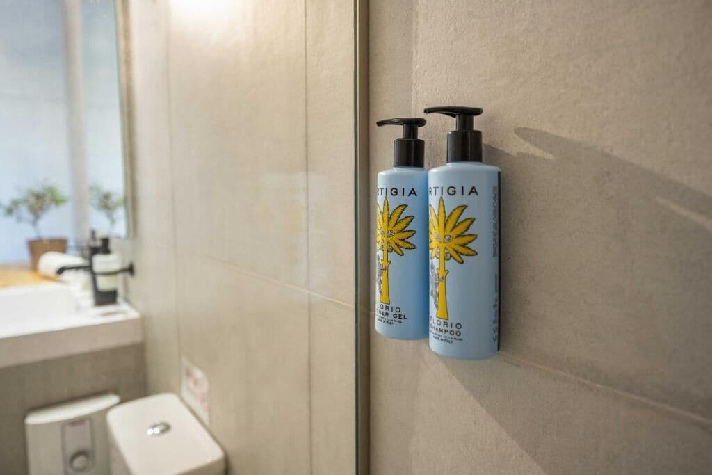 Zwei Flaschen 'ARTIGIA'-Haarpflegeprodukte an einer Badezimmerwand.