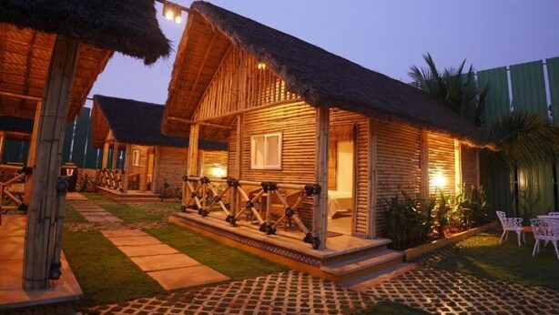 A wooden cabin with a thatched roof, a porch with railings, and a well-lit entrance.