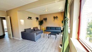 Ein Wohnzimmer mit grauem Sofa, blauem Sofa, Couchtisch aus Holz und gelbem Beistelltisch.