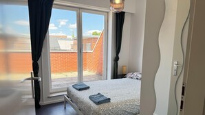 Ein Schlafzimmer mit Bett, einem Vorhangfenster, einer Tür und Blick auf ein Backsteingebäude.