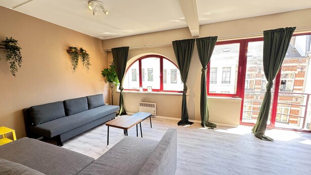 Ein modernes Wohnzimmer mit einer Couch, einem kleinen Tisch und Blick auf Gebäude durch große Fenster.