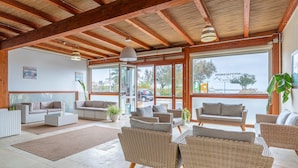 A spacious indoor area with wicker furniture, large windows, and a wooden ceiling. - Room 202 at 'Le Saline Rooms Marzamemi' with Wi-Fi and Air Conditioning (Marzamemi)