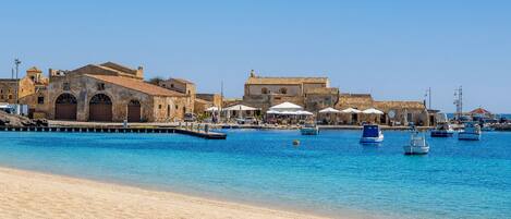 A coastal town with historic buildings, a sandy beach, and boats in the water.
