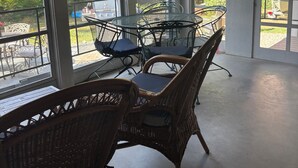 Eine überdachte Terrasse mit Korbstühlen, einem Tisch, großen Fenstern und einer amerikanischen Flagge.