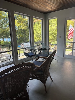 Eine überdachte Terrasse mit Korbstühlen, einem Tisch, großen Fenstern und einer amerikanischen Flagge.