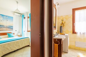 Quarto de hotel com cama, banheiro com pia e espelho, e janela com cortinas.