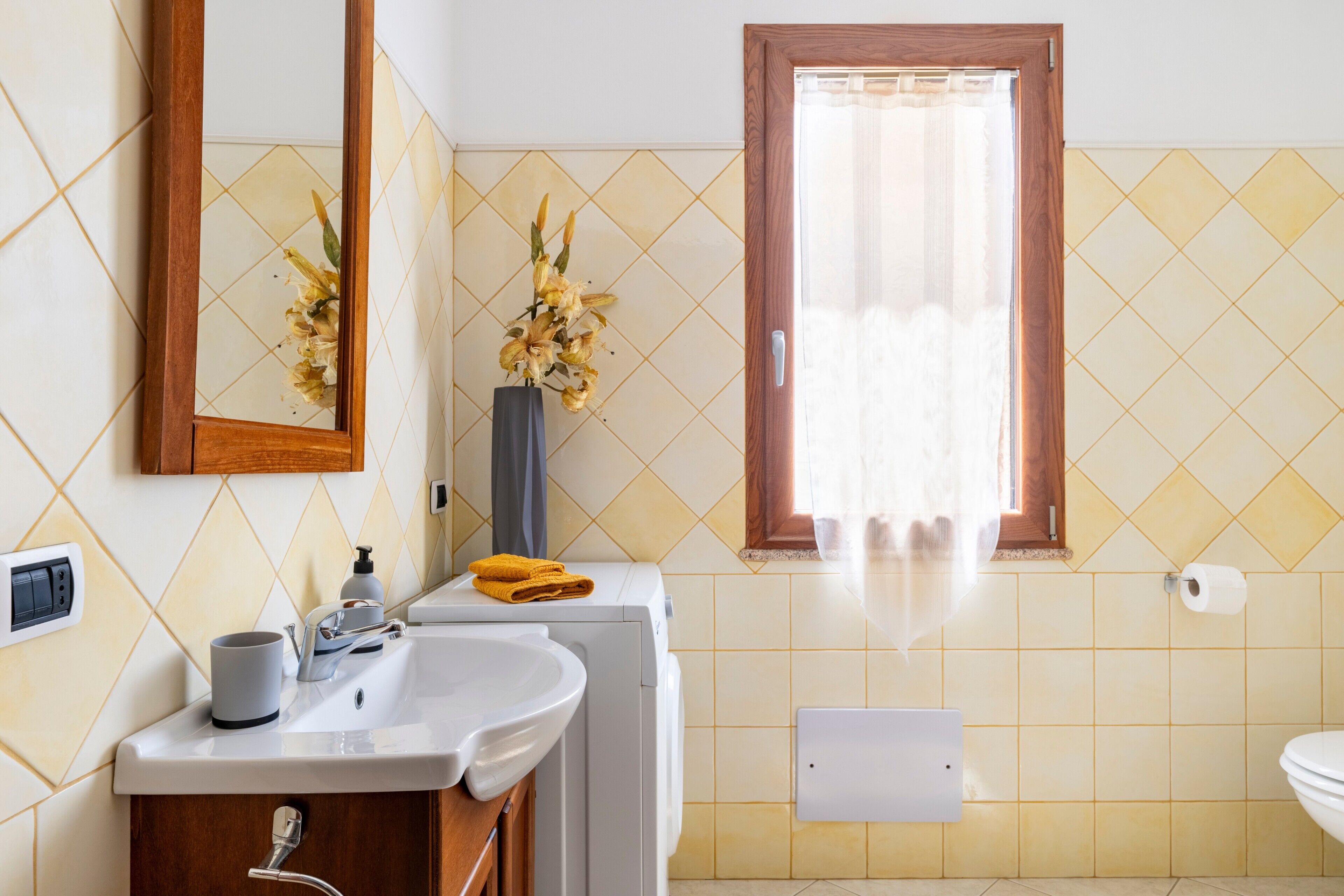 A bathroom with a sink, mirror, toilet, and a window with curtains.