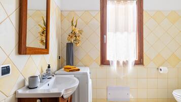 A bathroom with a sink, mirror, toilet, and a window with curtains.