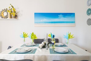 Mesa de jantar posta com pratos, talheres e objetos decorativos, com uma pintura representando uma cena de praia acima.