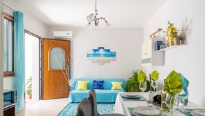 Un coin repas avec une table dressée pour quatre personnes, un canapé bleu orné de coussins à motifs, un lustre et une étagère murale décorative.